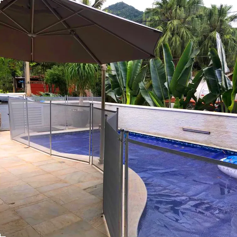 Cerca removível para piscina instalada em área com guarda sol e jardim tropical